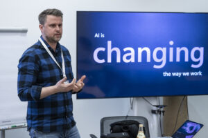 Ein Mann gestikuliert neben einem großen Monitor