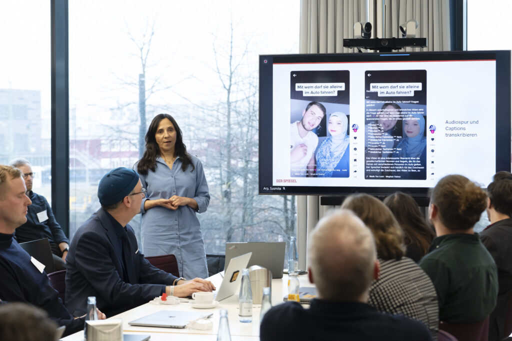 Eine Frau während einer Präsentation in einem Konferenzraum. Rechts neben ihr ein Monitor.