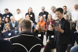 Eine gestikulierende Frau in einem Konferenzraum mit Menschen
