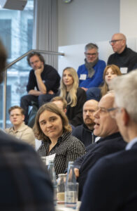 Eine Frau hört einem Mann zu, der spricht. Im Hintergrund sind Menschen in einem Konferenzraum zu sehen.