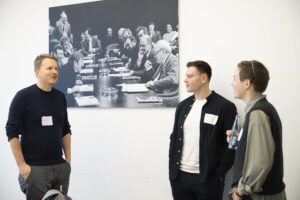 Drei Personen im Gespräch, im Hintergrund ein Foto aus einer SPIEGEL-Redaktionskonferenz.