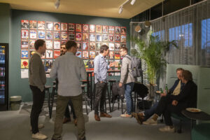 7 Menschen in einer Lounge. An der Wand sind Zeitschriften-Cover zu sehen